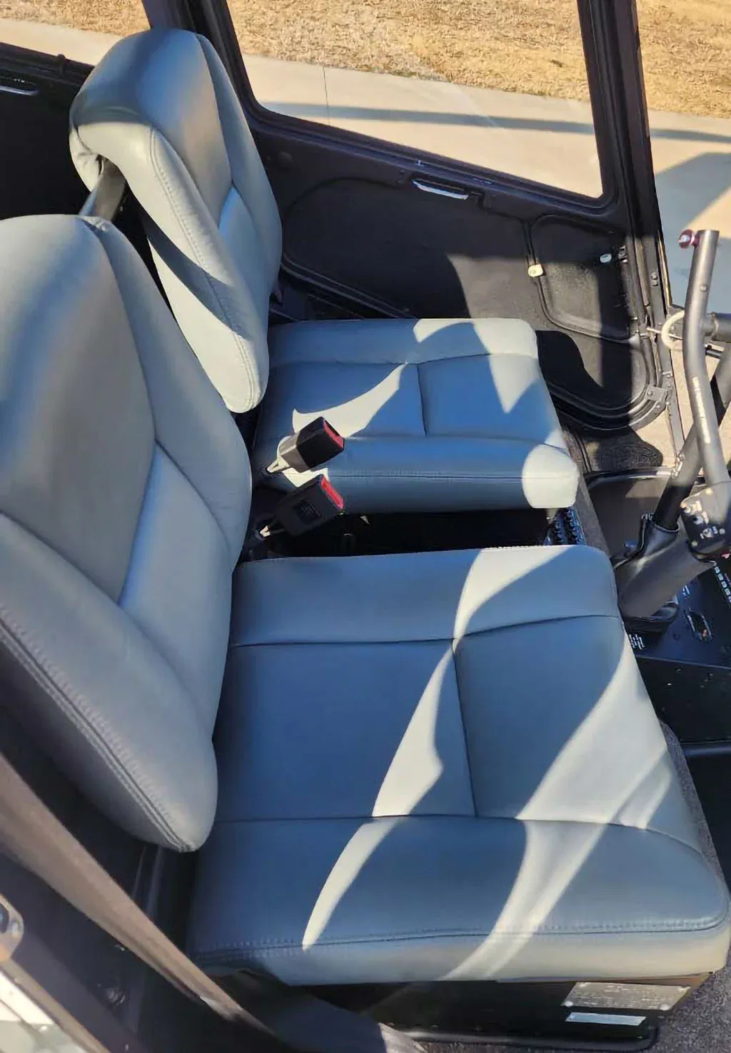 The gray leather front and rear seats of a helicopter interior are illuminated by sunlight.