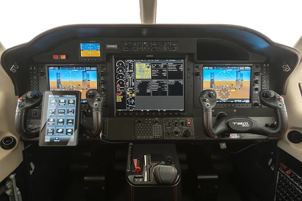 The cockpit of a Daher TBM 900 aircraft, featuring a modern glass panel with multiple Garmin displays and a tablet mount.
