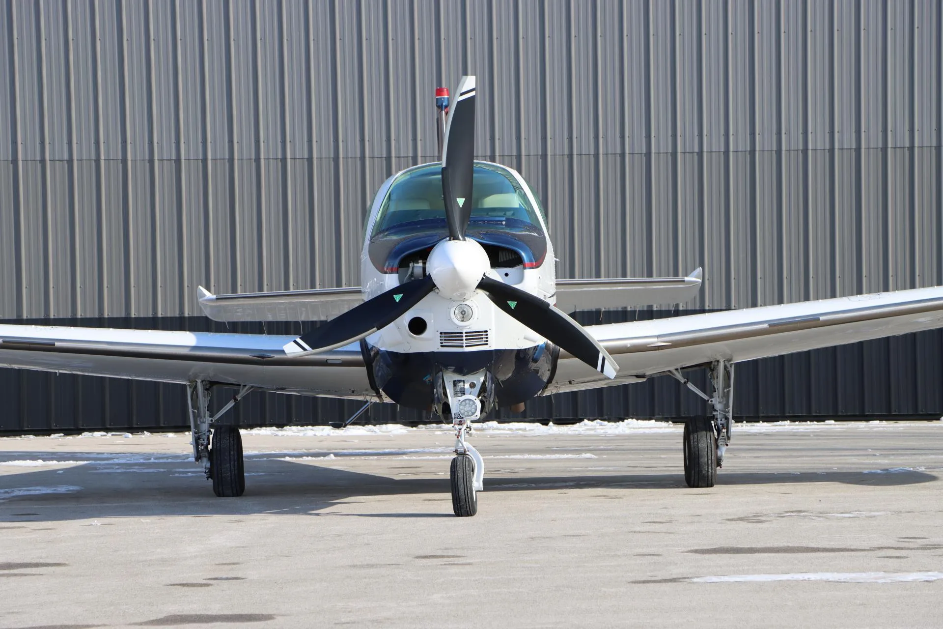 Close-up front view of a white, blue, and red single-engine aircraft with a three-blade propeller.