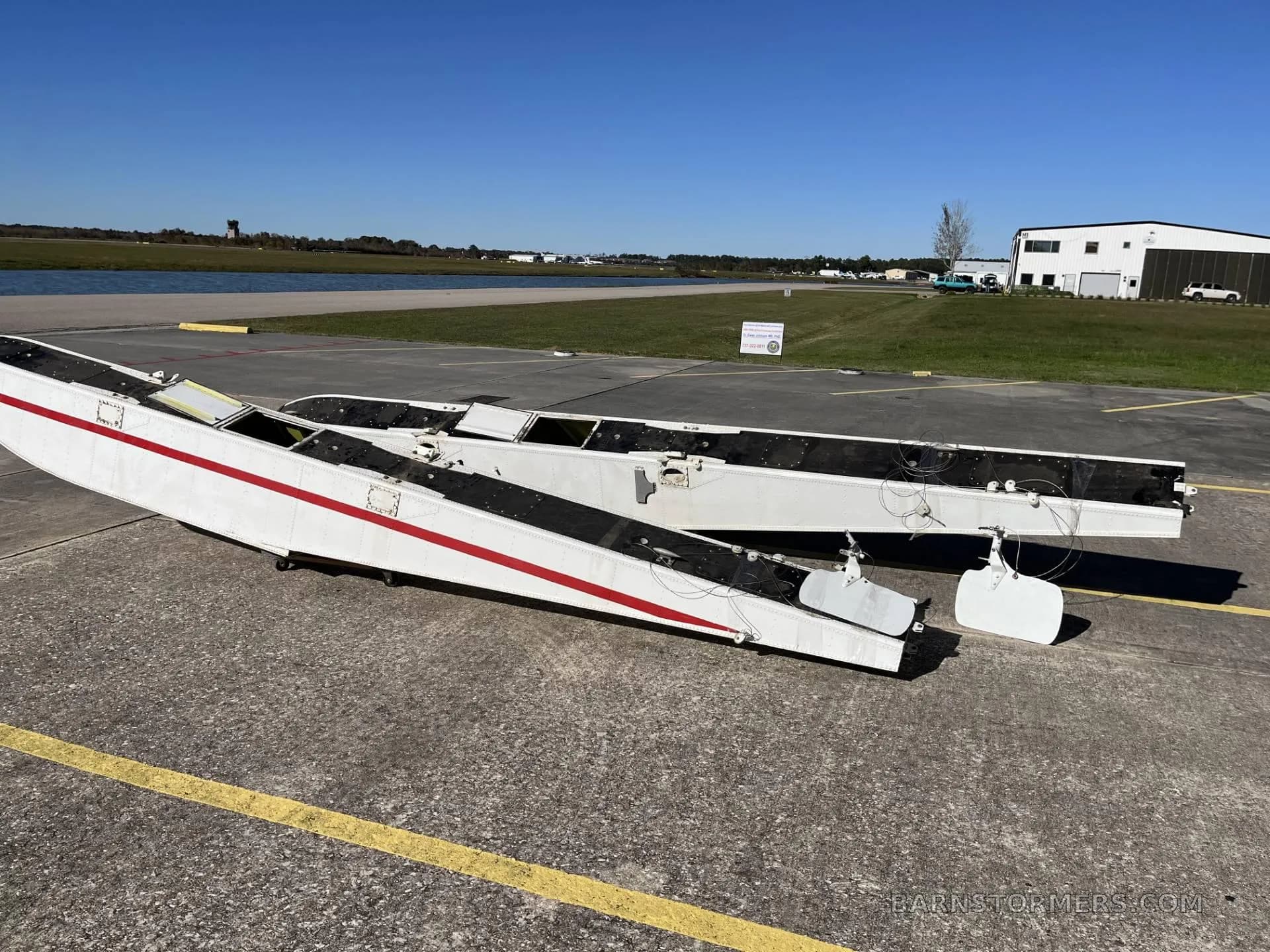 Two white aircraft floats with red stripes lying on a concrete runway or taxiway with buildings in the background.