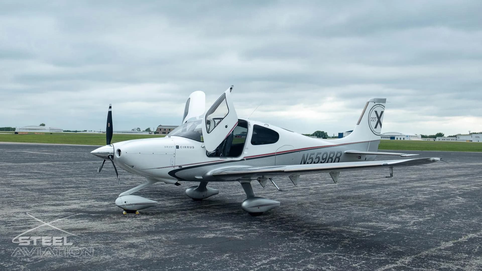 A white and silver Cirrus SR22T aircraft with registration N559RR has its gull-wing doors open on an airfield.