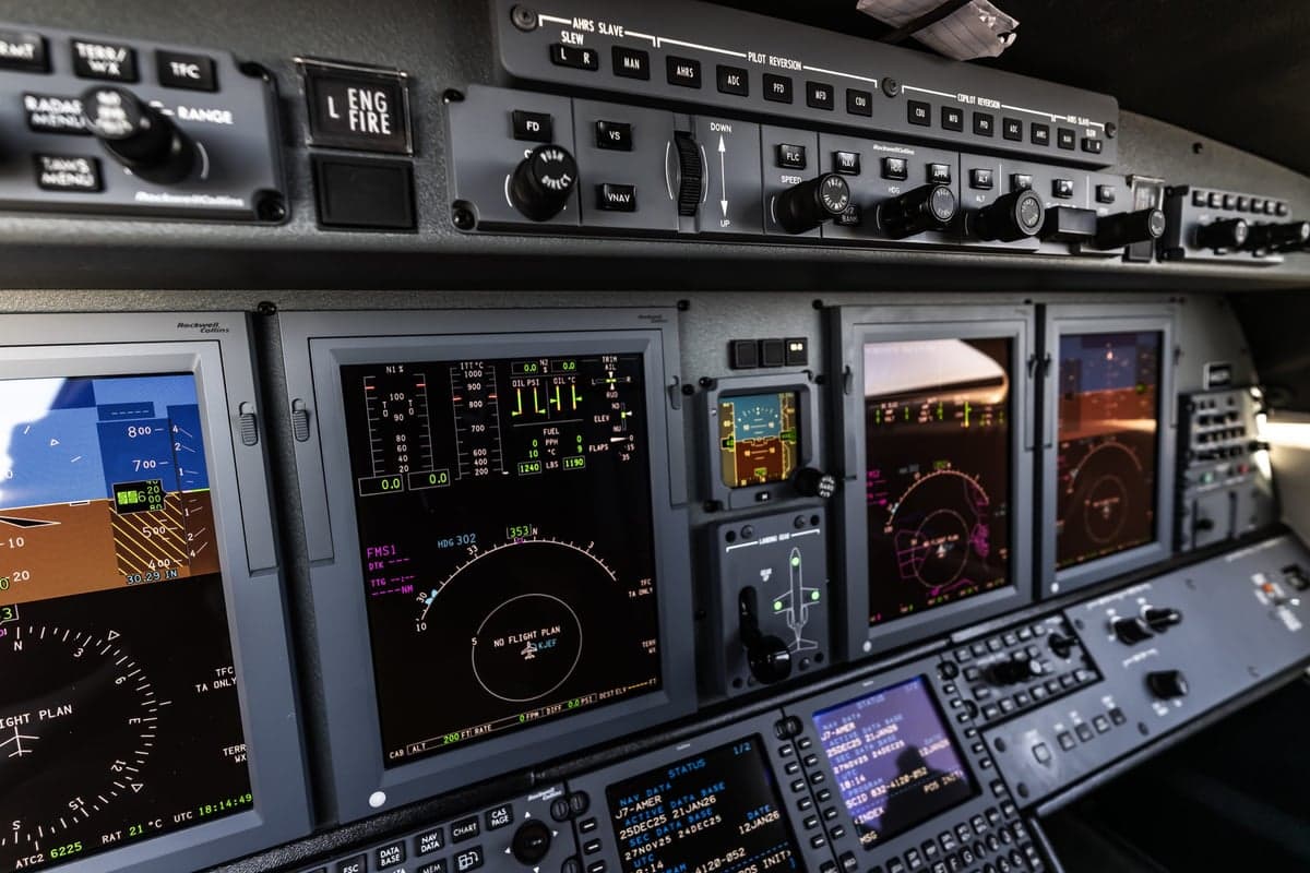A detailed view of a modern aircraft cockpit with multiple digital displays showing flight information and controls.