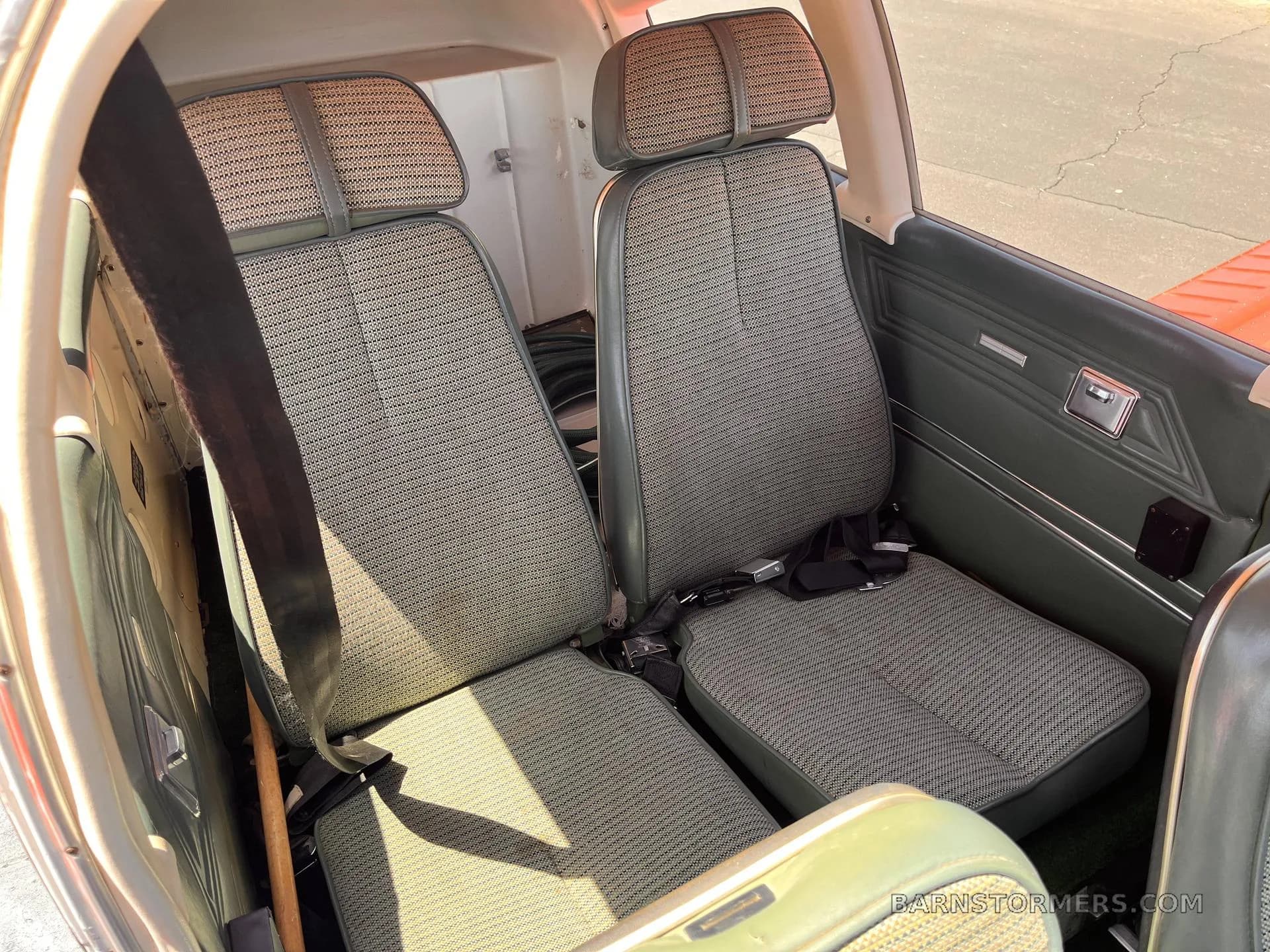 The front two green patterned fabric seats of an aircraft interior, with seatbelts visible.