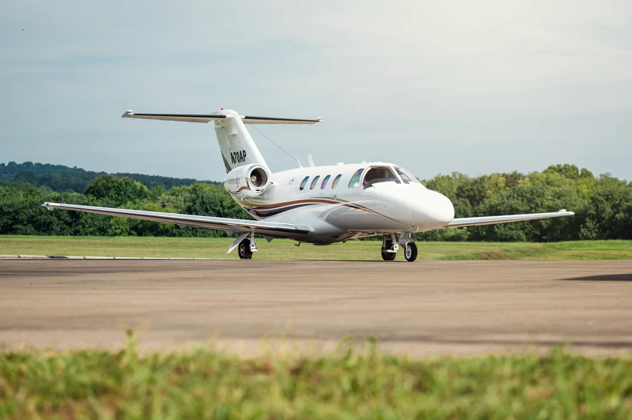A white Cessna Citation business jet with brown and gold stripes, tail number N70AP, parked on an airfield.