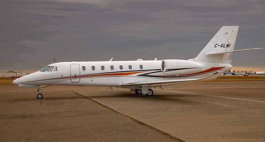 A white business jet with orange and black stripes on the fuselage, parked on an asphalt tarmac under a cloudy sky.