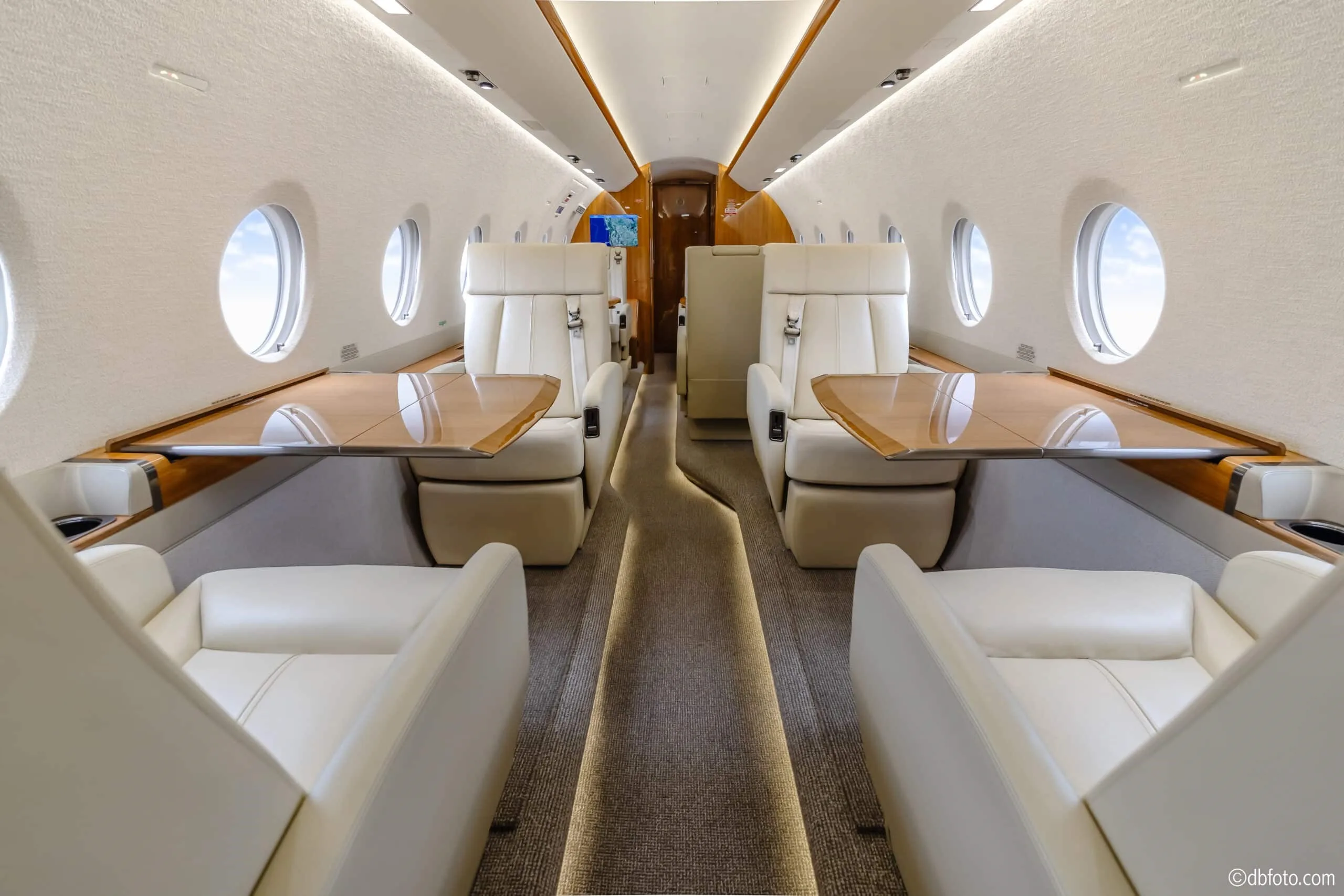 The aircraft cabin with cream leather seats facing each other, featuring pull-out wooden tables.