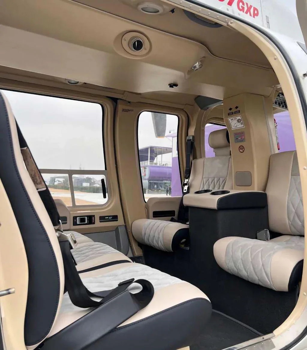 The spacious beige and gray interior of a helicopter cabin, looking towards the rear seats and out a window.