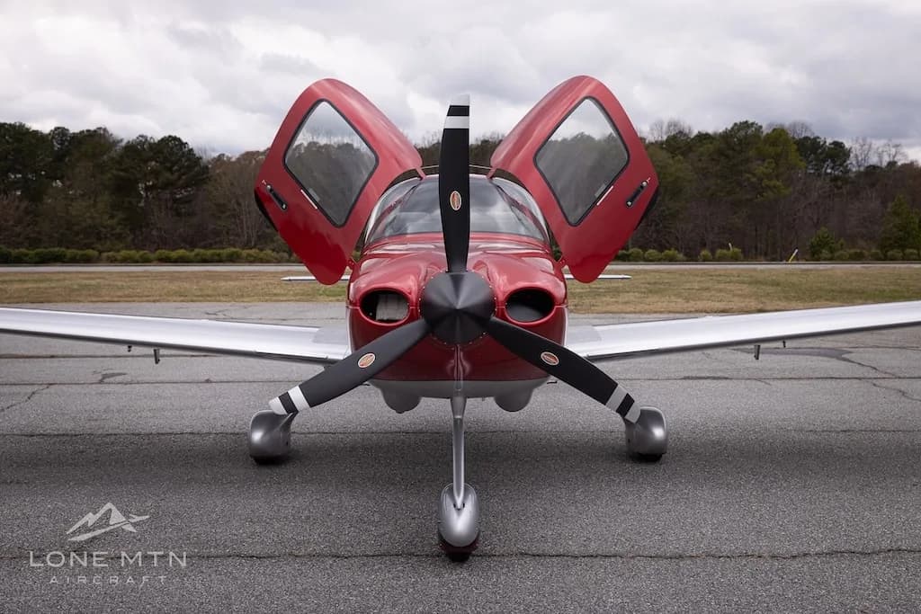 A head-on view of the red and silver Cirrus Vision Jet (N428CC) with its gull-wing doors open, parked on an asphalt tarmac.