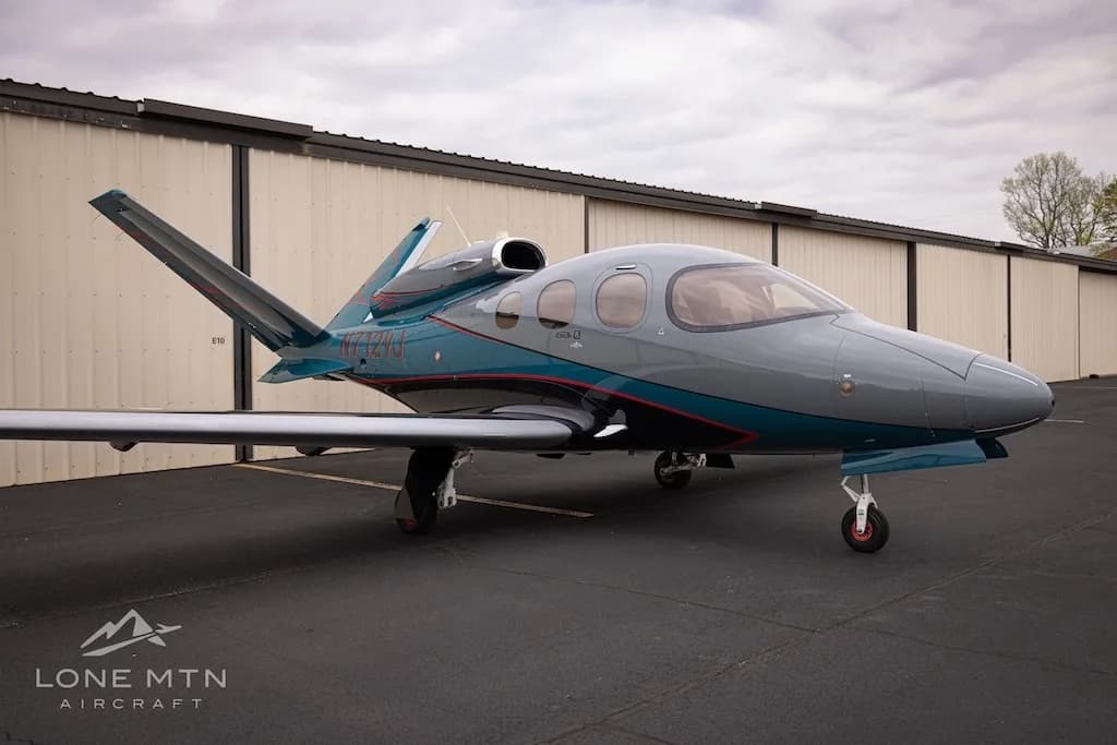 A front-side view of the Cirrus Vision Jet (N712VJ) in grey and teal, parked on an airfield.