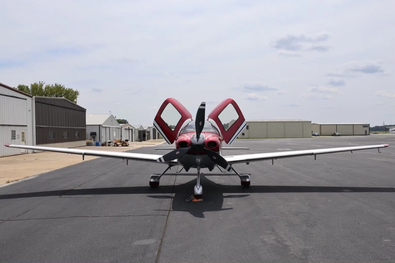 A front view of the red and silver Cirrus SR22T aircraft with its doors open, parked on an airfield.