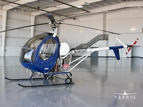 A blue and white Schweizer 300C helicopter, registration N3624T, parked in a hangar.