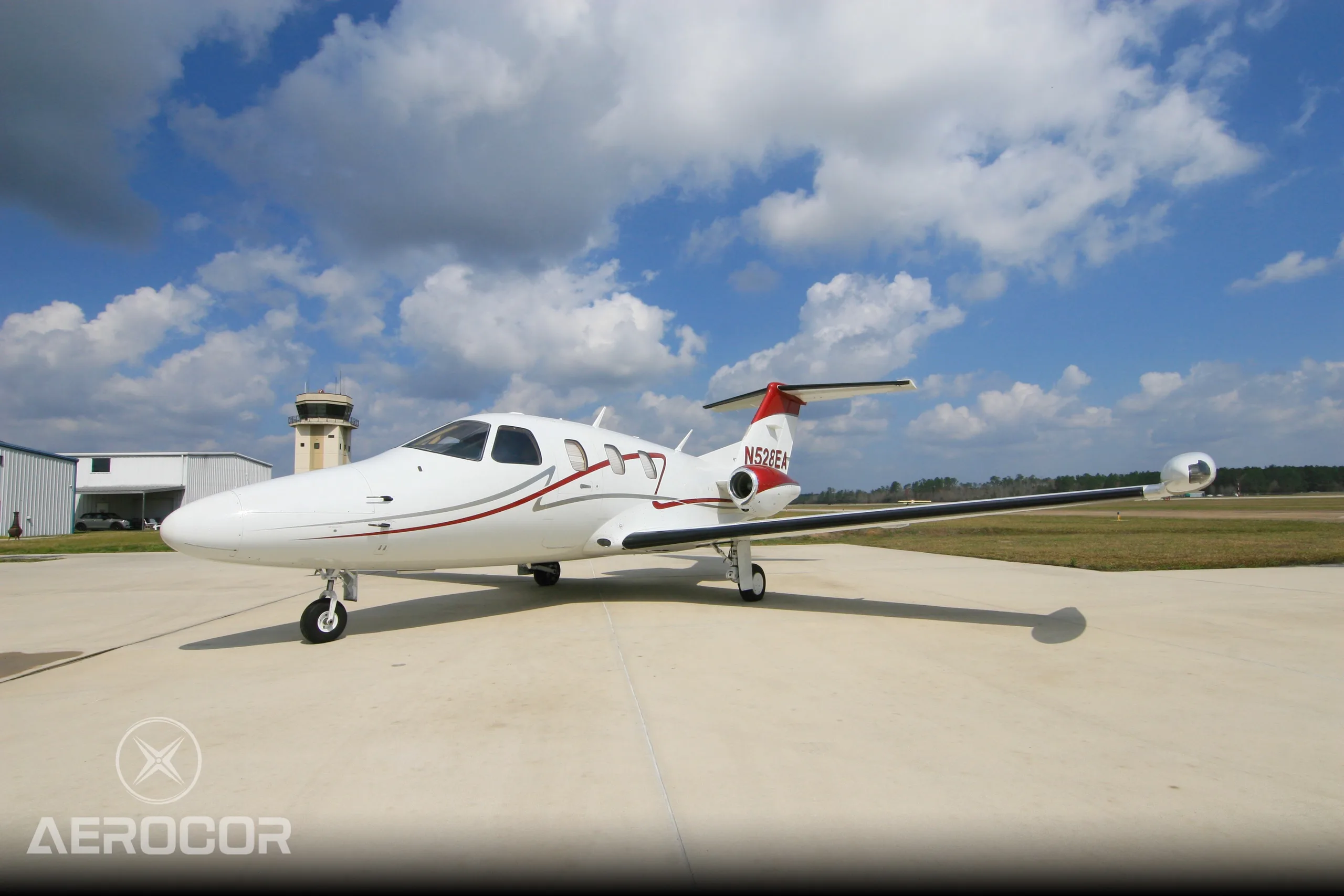 A white Eclipse 500 jet with red and grey stripes, registration N528EA, parked on an airport tarmac with a control tower in the background.