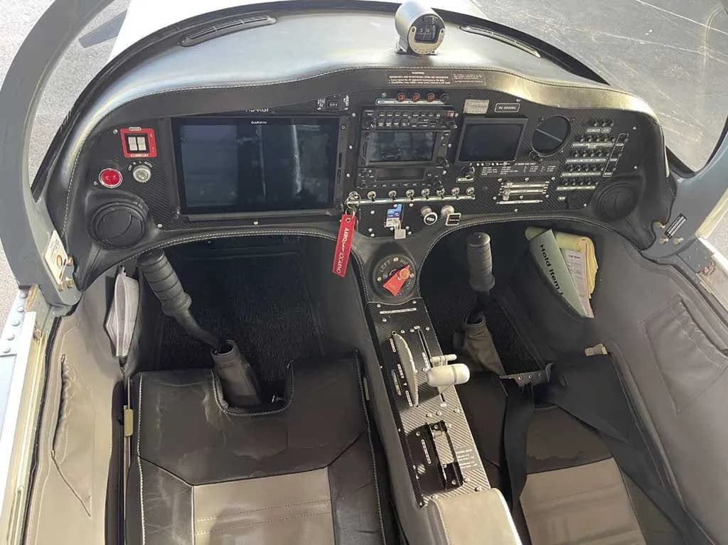 The cockpit of a Sonaca 200 aircraft, showing the instrument panel with screens, controls, and two-tone seats.