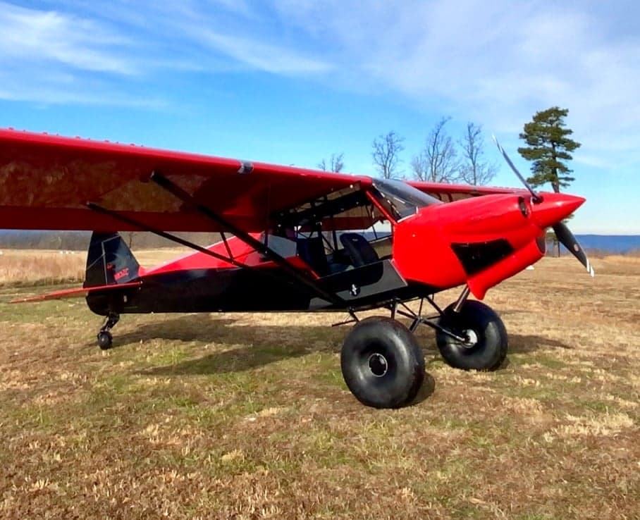 Side view of the red and black N83ZC aircraft parked on a grassy field.