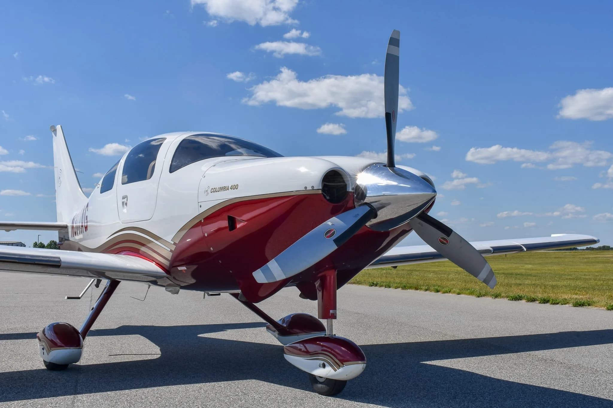 Front three-quarter view of a white and maroon Columbia 400 aircraft parked on an airfield.