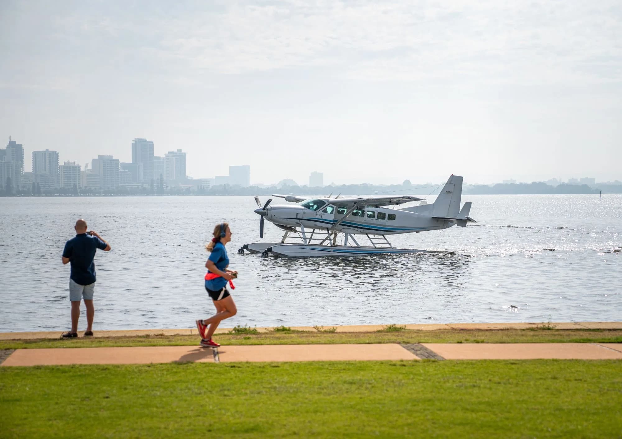 A seaplane on the water with people walking along the shore.