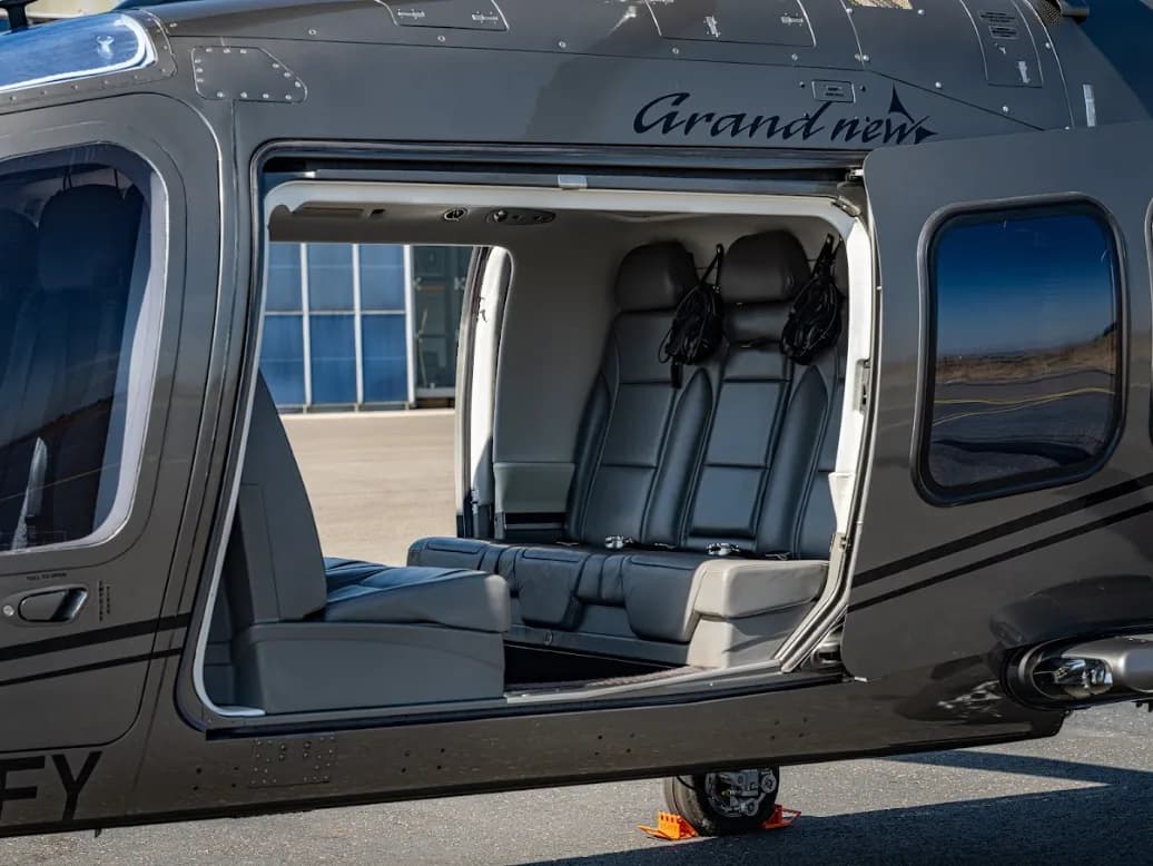 The open passenger door of a grey AgustaWestland AW109 GrandNew helicopter reveals its grey leather interior seats.