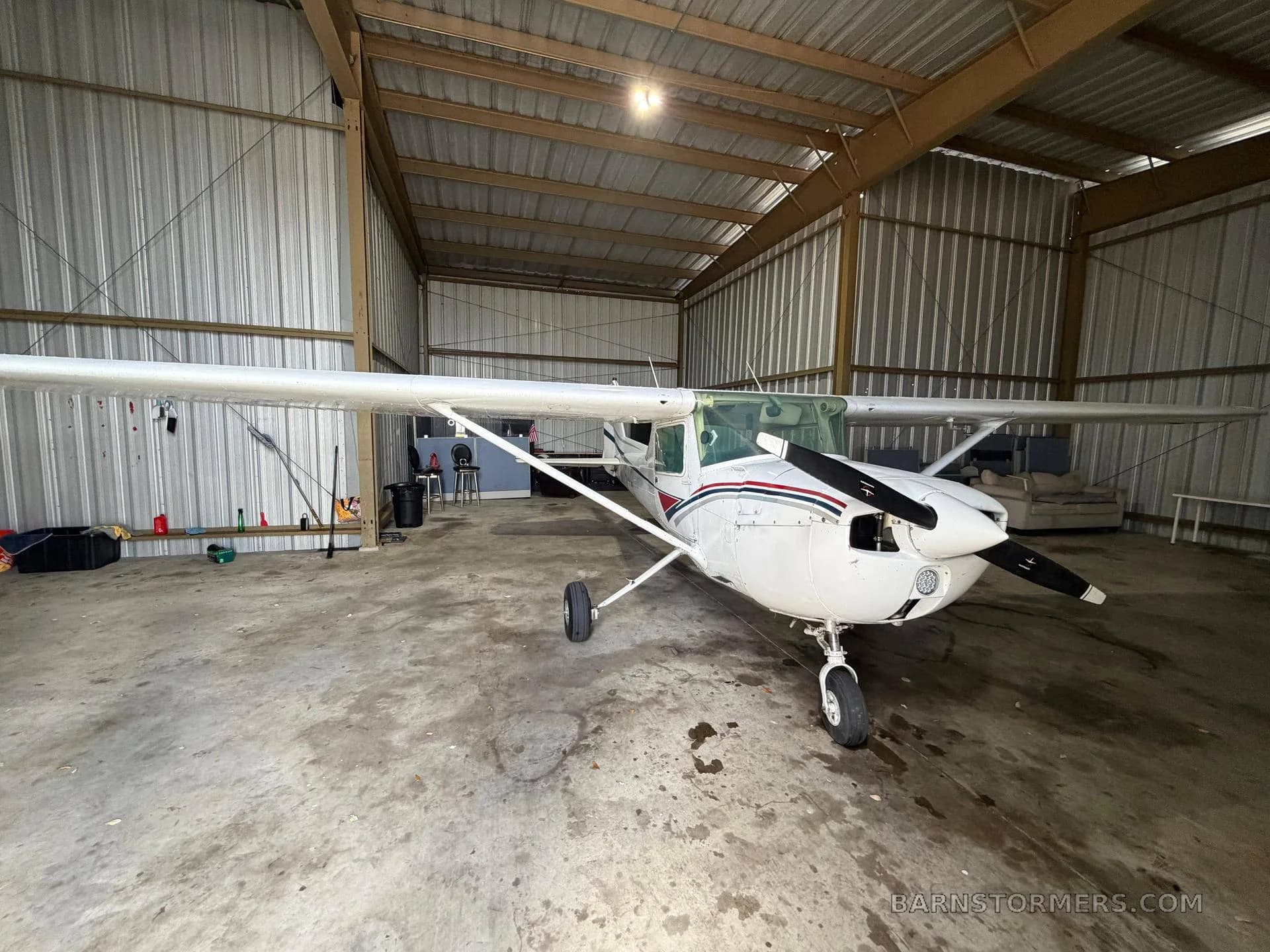 A white Cessna 172 with red and black stripes parked inside a metal hangar.