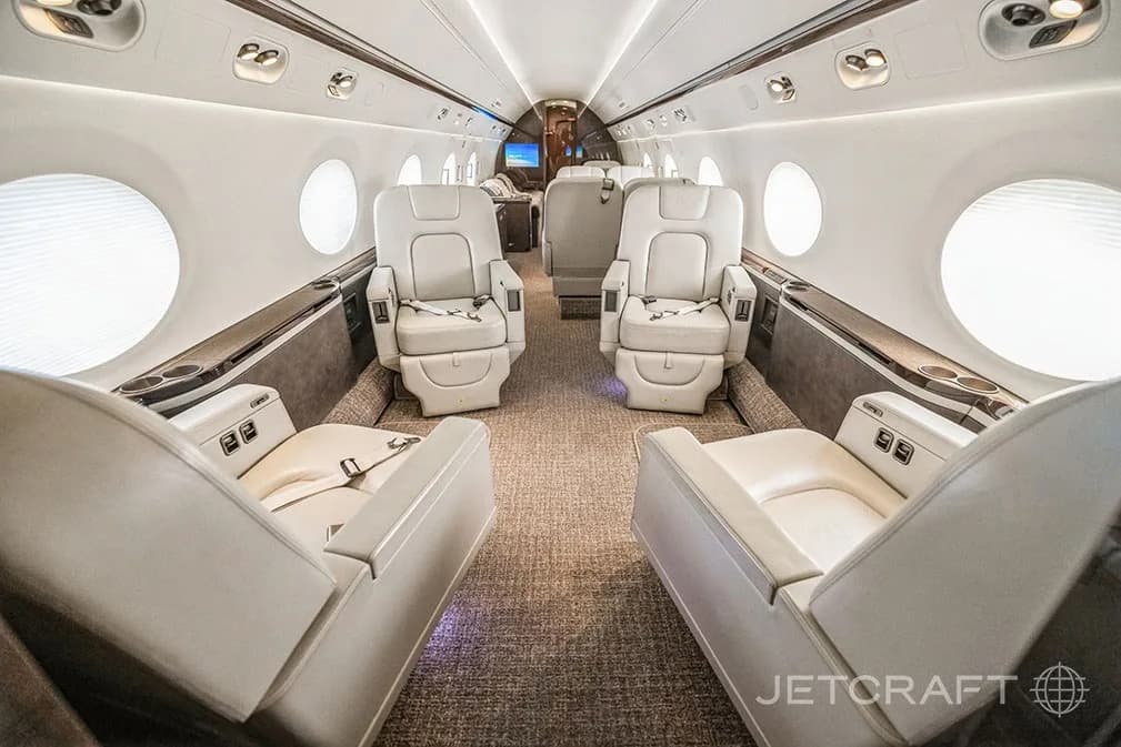 A spacious aircraft cabin featuring two sets of facing light-colored leather seats with seatbelts.