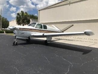 A Beechcraft Bonanza sits on the tarmac in front of a building.