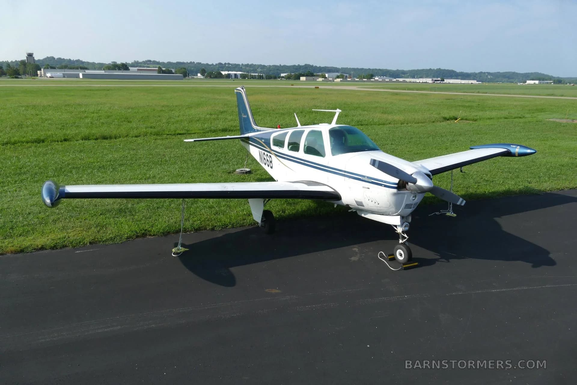 An aerial view of a white and blue Beechcraft Bonanza (N166B) parked on an airport tarmac.
