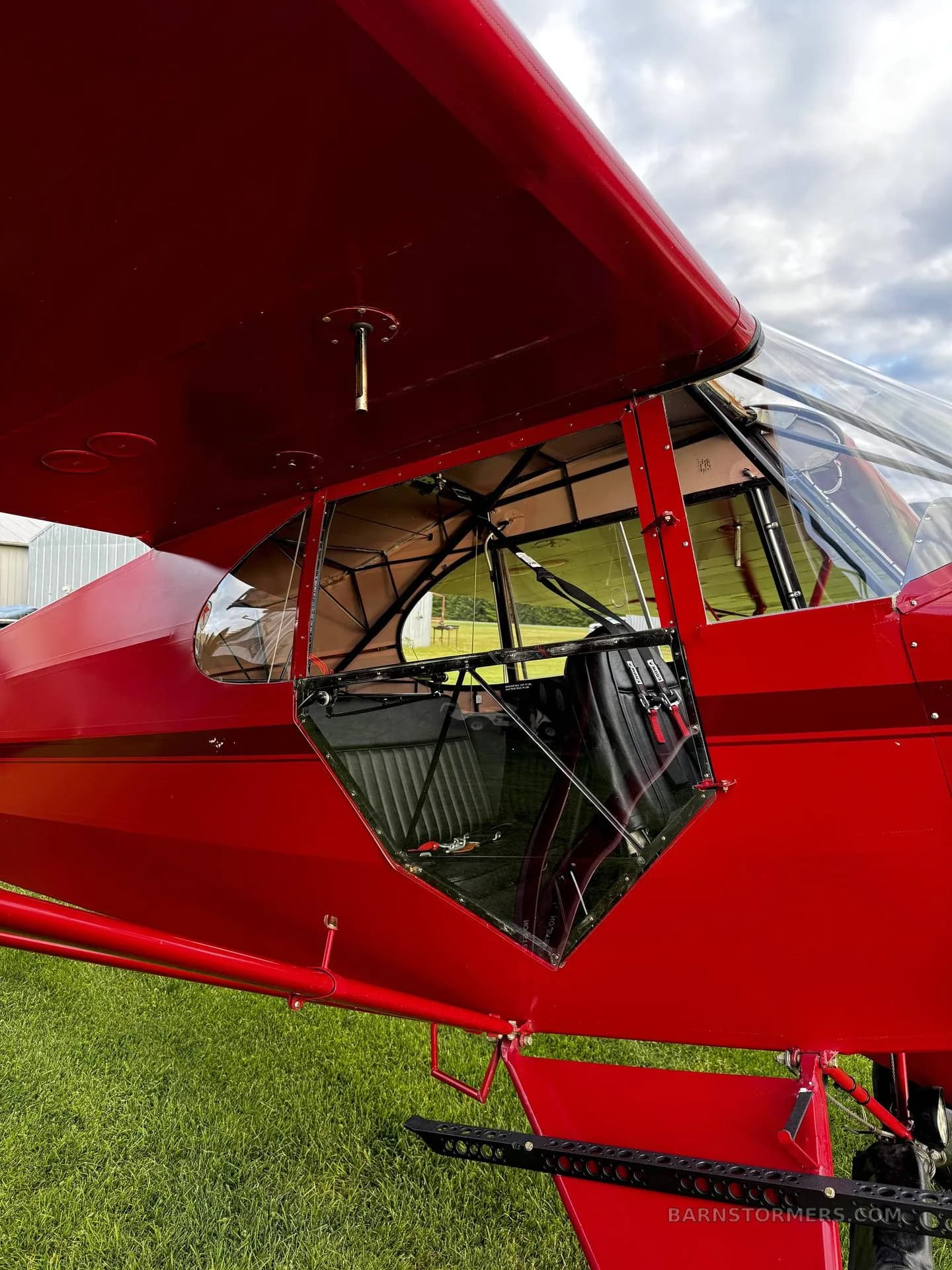 A close-up view of the red Piper Cub's open door and side window, revealing part of the interior and seat.