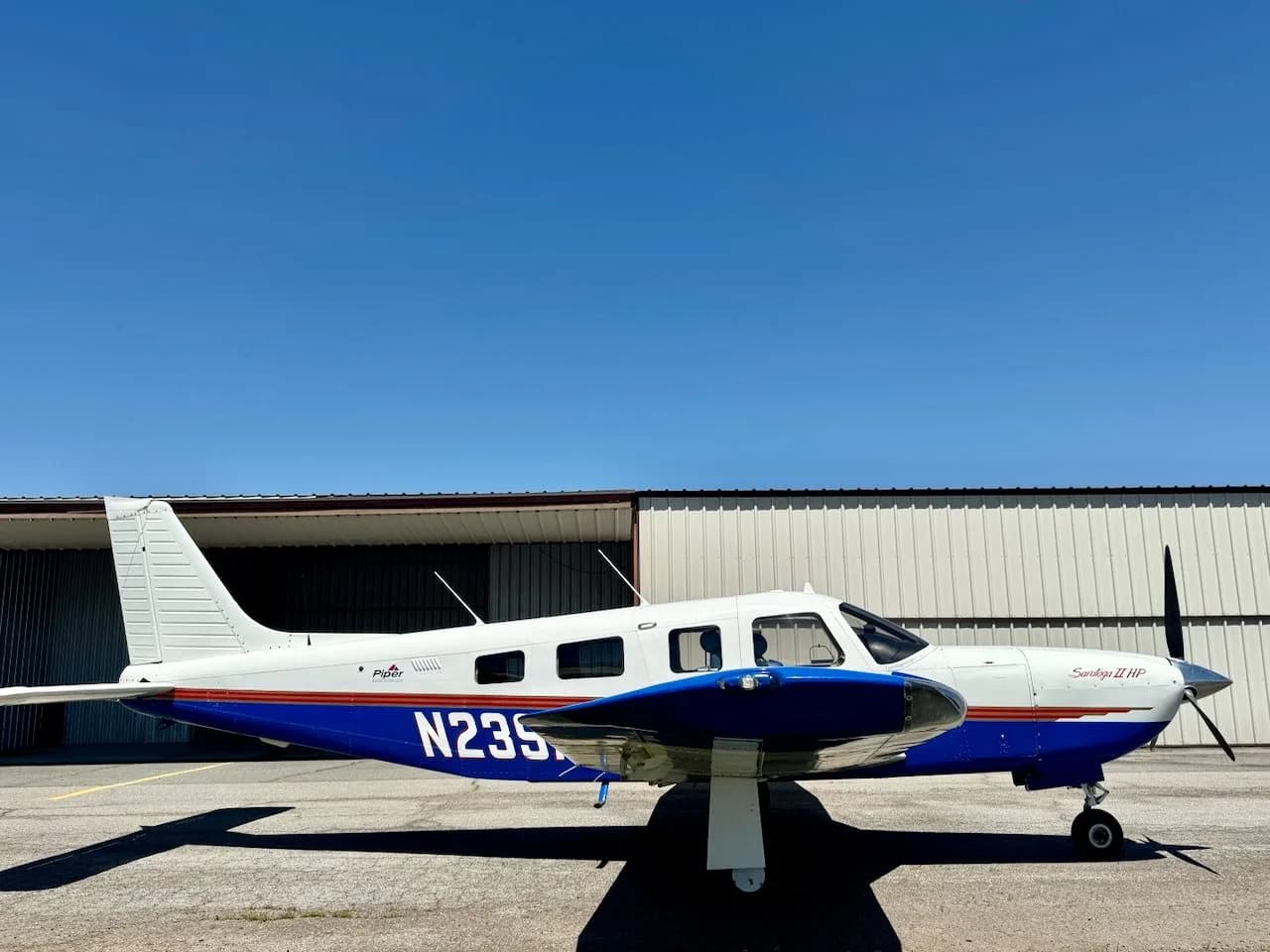 A side view of a white and blue Piper Saratoga II HP aircraft with registration N235, parked on an airfield.