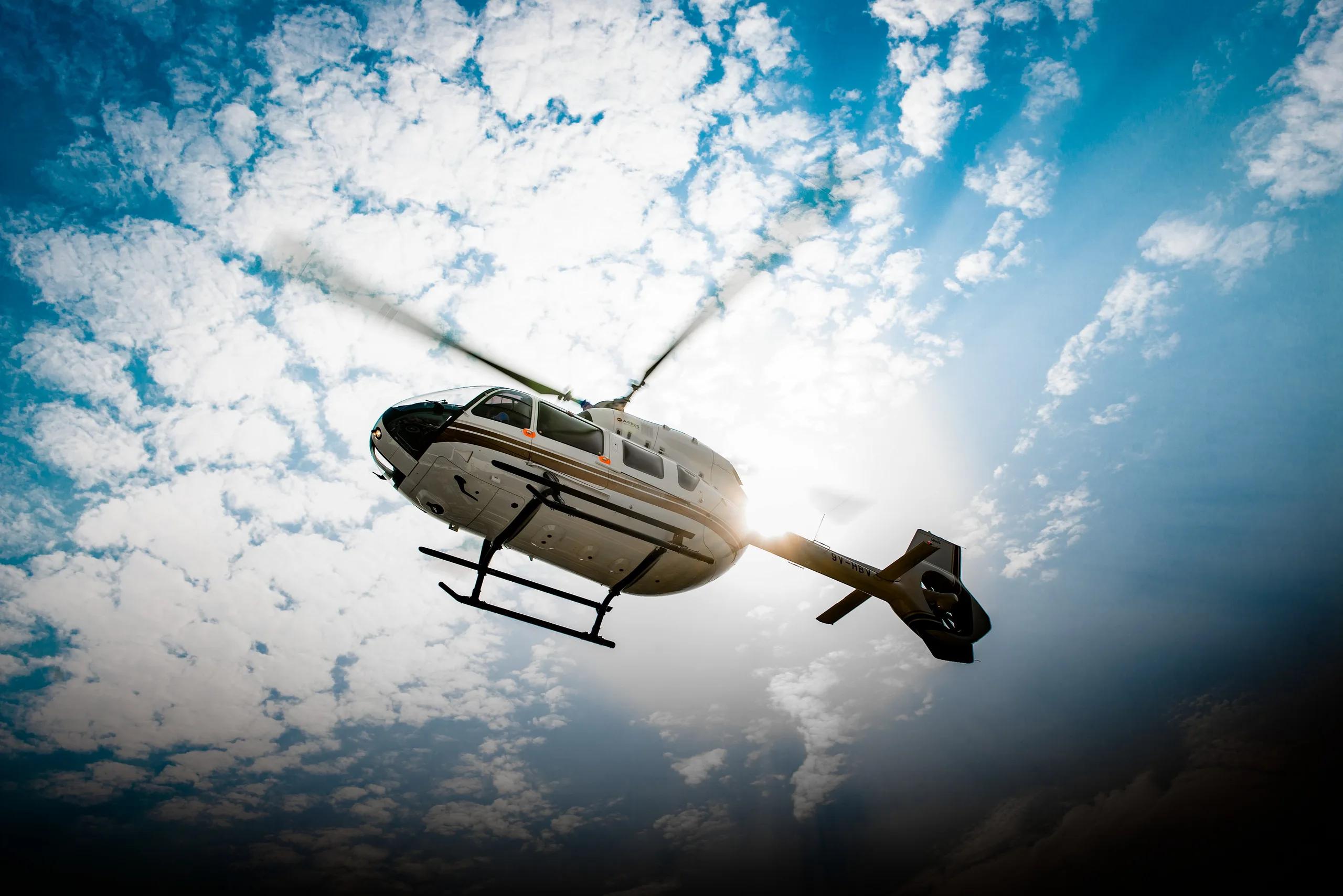 A white and gold helicopter flying in front of a cloudy sky.