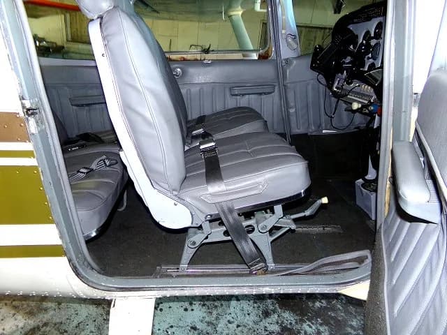 The gray leather front and rear cabin seats of a Cessna 182, viewed from the open door.