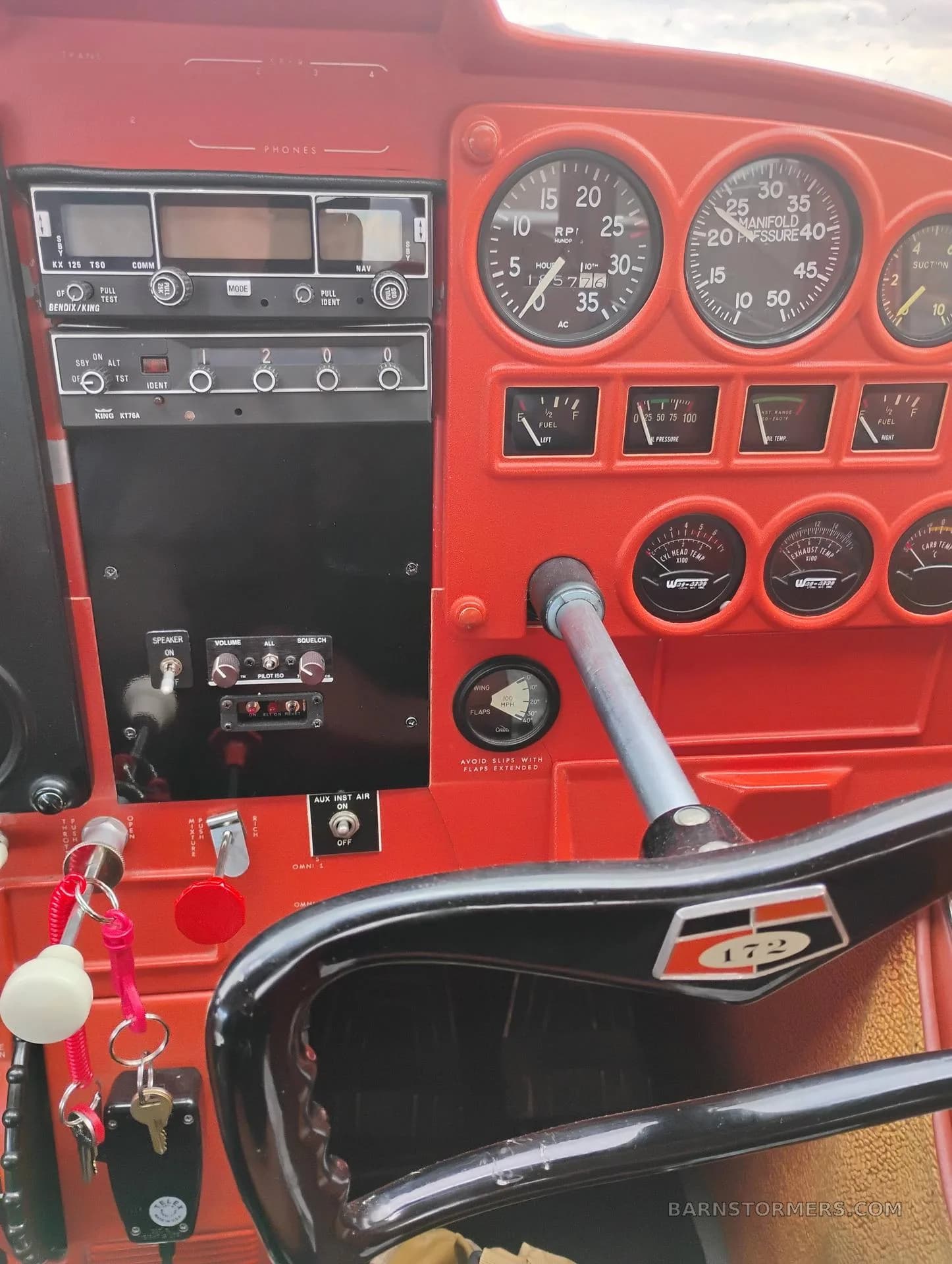 A detailed view of the red instrument panel, avionics stack, and yoke of a Cessna 172 aircraft.