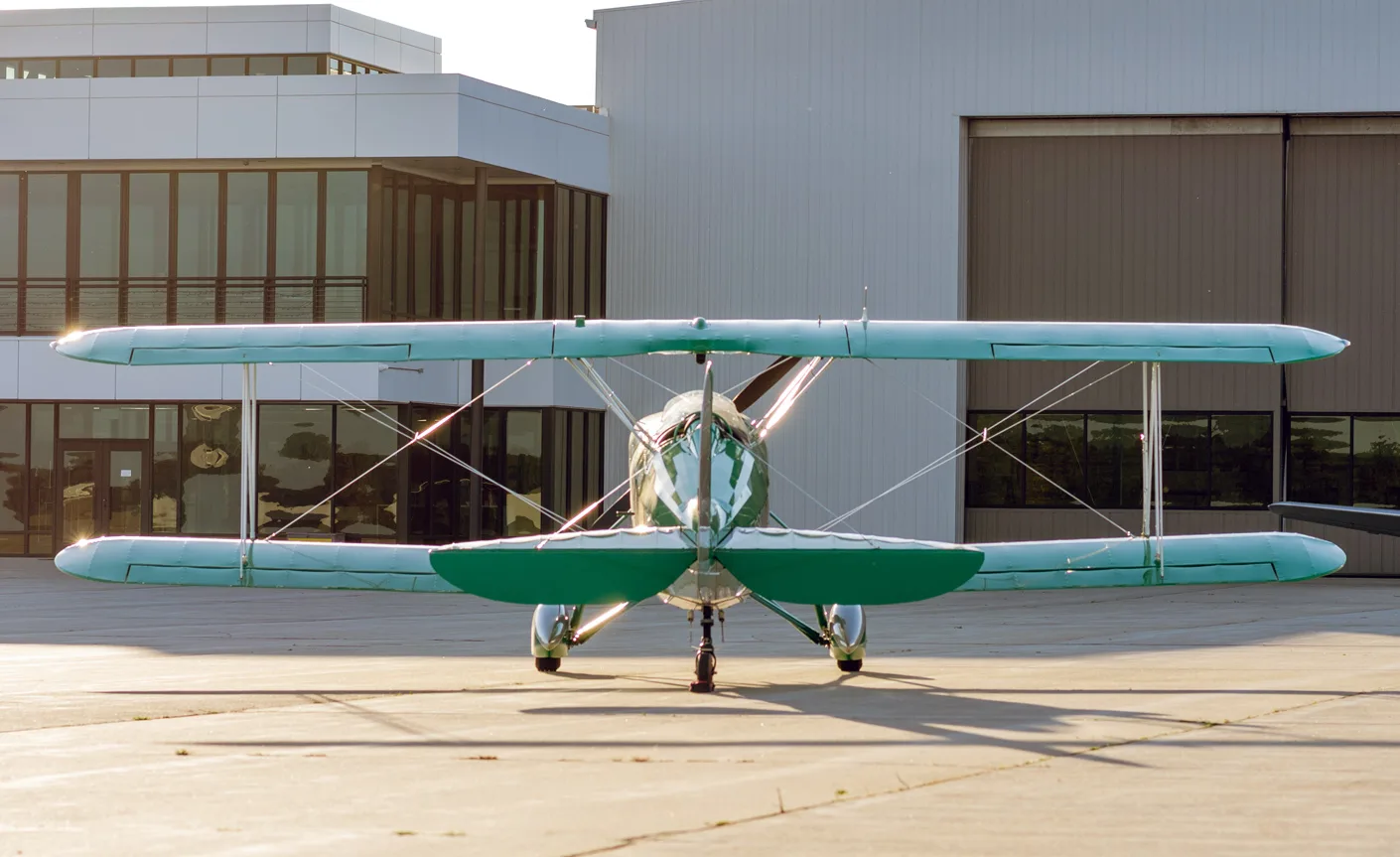 Rear view of the green and silver biplane parked in front of a modern building.
