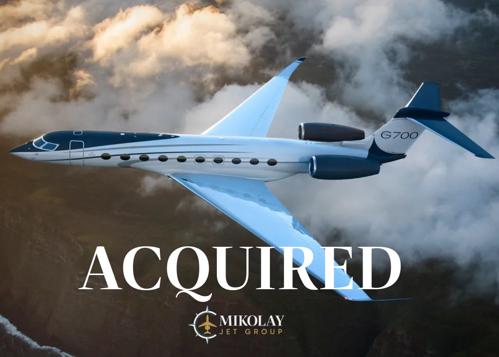 A Gulfstream G700 business jet with a dark blue and white paint scheme flying over clouds.