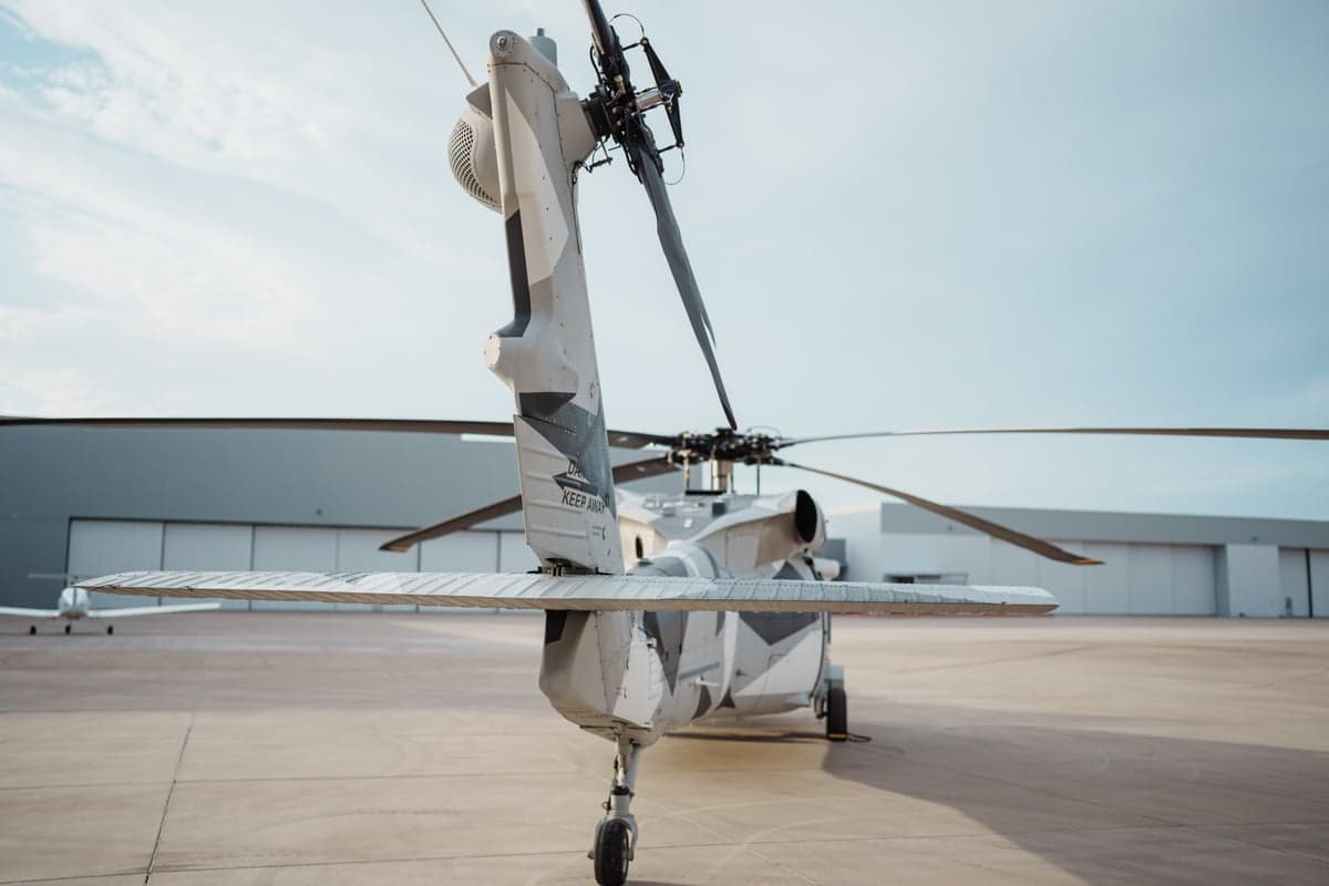 Rear view of a Sikorsky S-70i helicopter with a gray camouflage paint scheme on the tarmac.