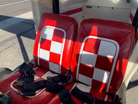 Two red and white checkered aircraft seats with seatbelts in the cabin interior.