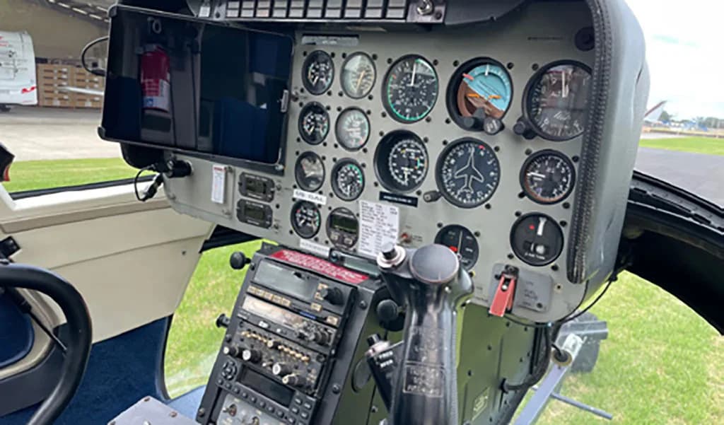 The helicopter cockpit showing the instrument panel with multiple gauges and a control stick.