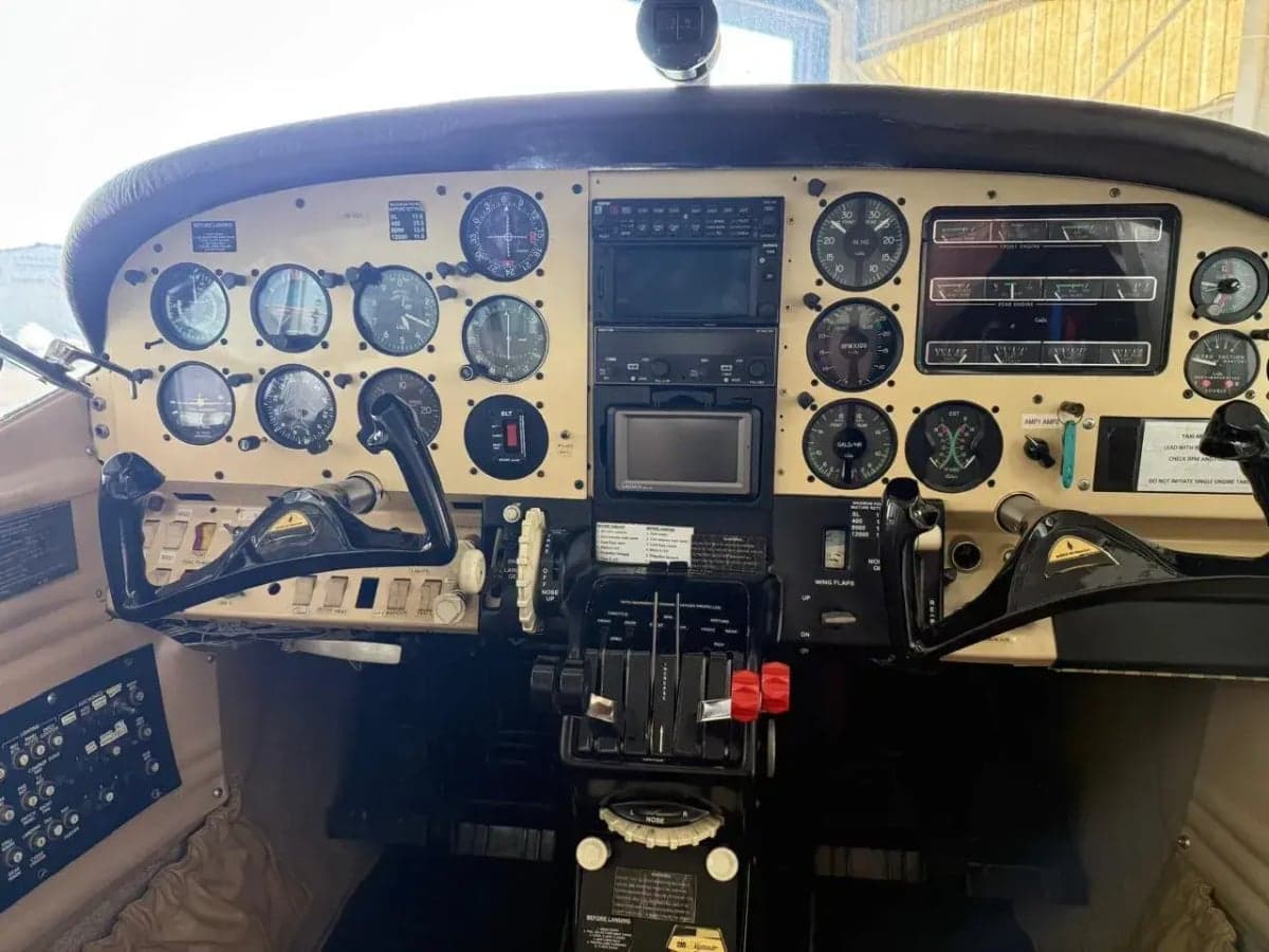 View of an aircraft cockpit with a beige instrument panel filled with analog gauges and some digital displays.