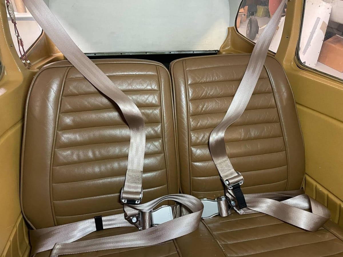 Two brown leather aircraft seats with seatbelts, viewed from inside the cabin looking towards the rear.