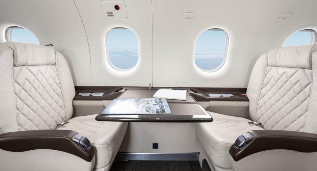 Interior view of the aircraft cabin with white leather seats and a table.
