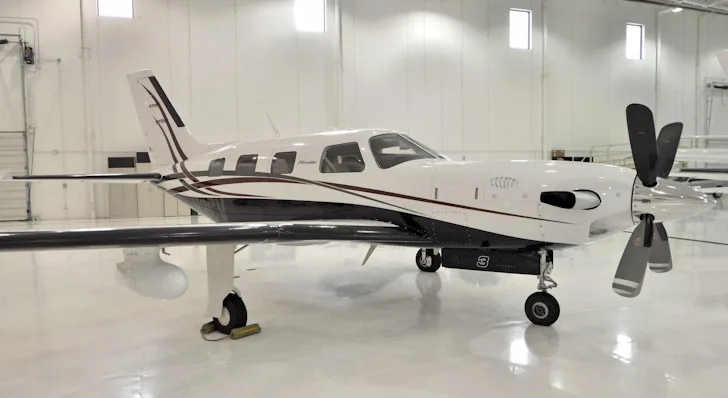 A white and black Piper Meridian aircraft with red accents, registration N3CV, parked in a brightly lit hangar.