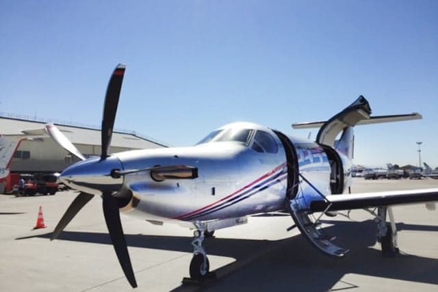 A Pilatus PC-12 aircraft is parked on the tarmac with its door open.