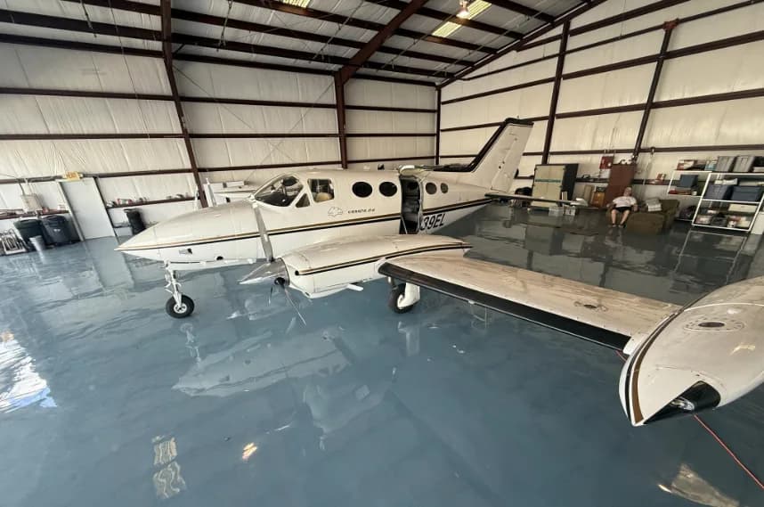 A white Cessna 414 aircraft with gold and black stripes and registration N239EL, parked in a hangar with its passenger door open.