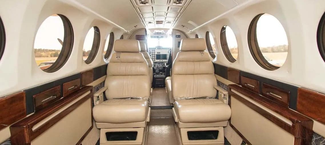 A view down the aisle of the Beechcraft King Air 200 cabin, showing the leather seats and wood trim.