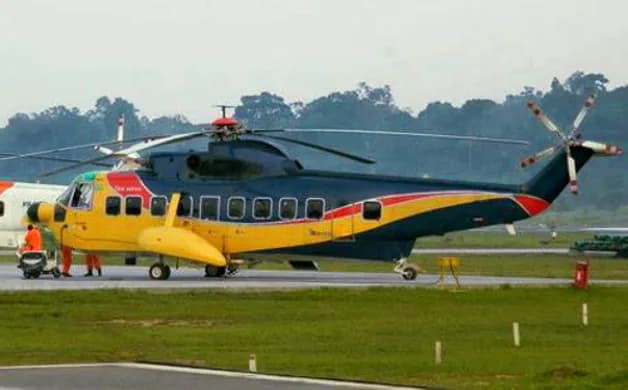 A large, dark blue and yellow helicopter with red accents is parked on an airfield, with a person near the front.