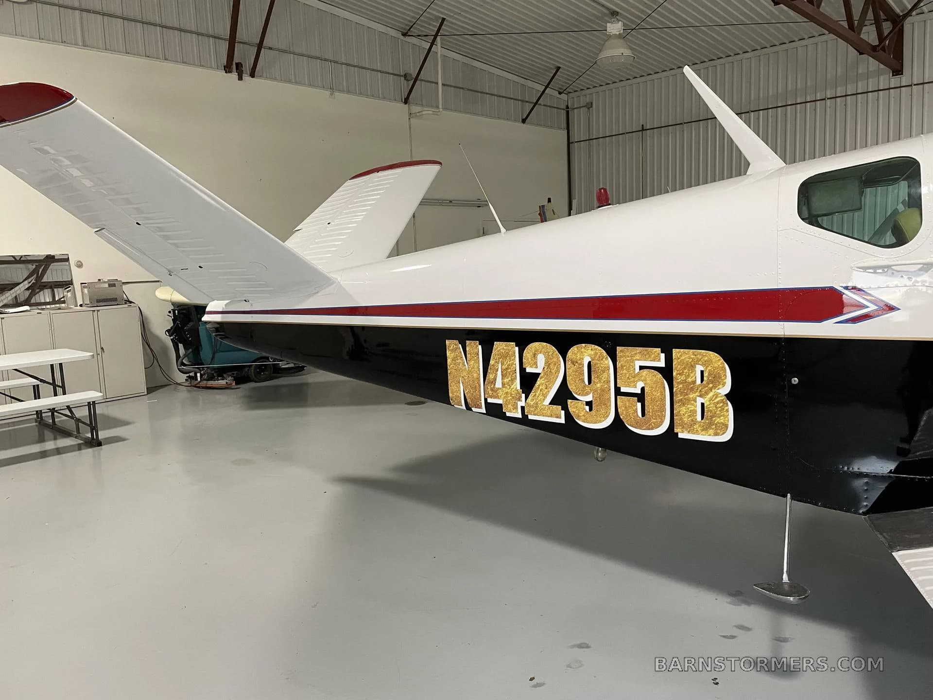 A side view of the tail and rear fuselage of a white and black aircraft with gold registration N14295B in a hangar.