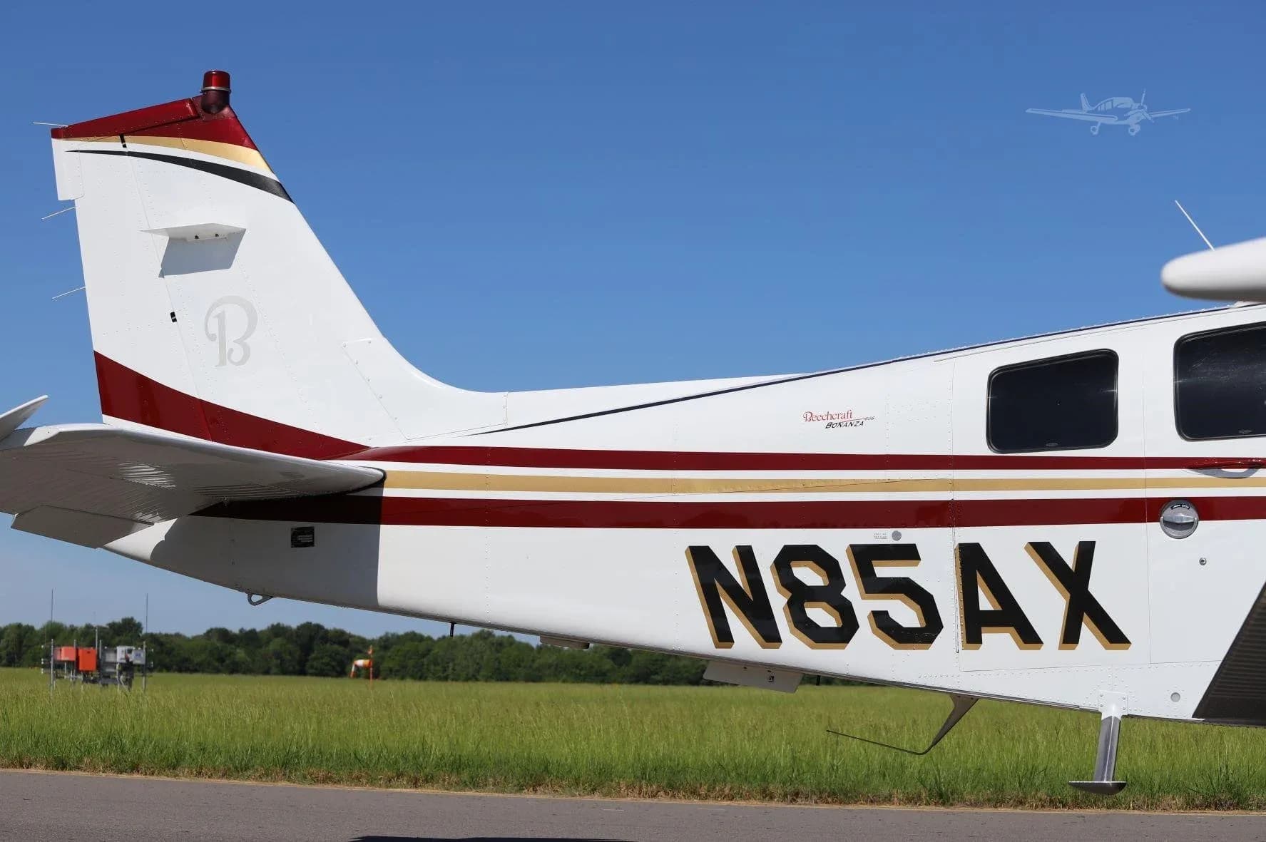 A close-up view of the tail section of a white aircraft with red and gold stripes, showing the registration N85AX.