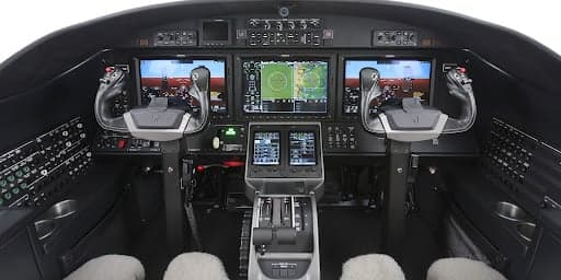 The modern cockpit of the Cessna Citation CJ3+ featuring multiple digital displays, flight controls, and a central throttle quadrant.