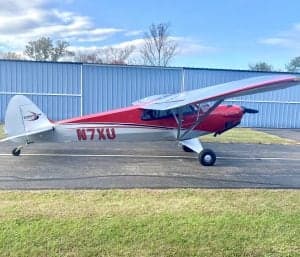 Side view of the red and silver Carbon Cub N7XU on the tarmac.