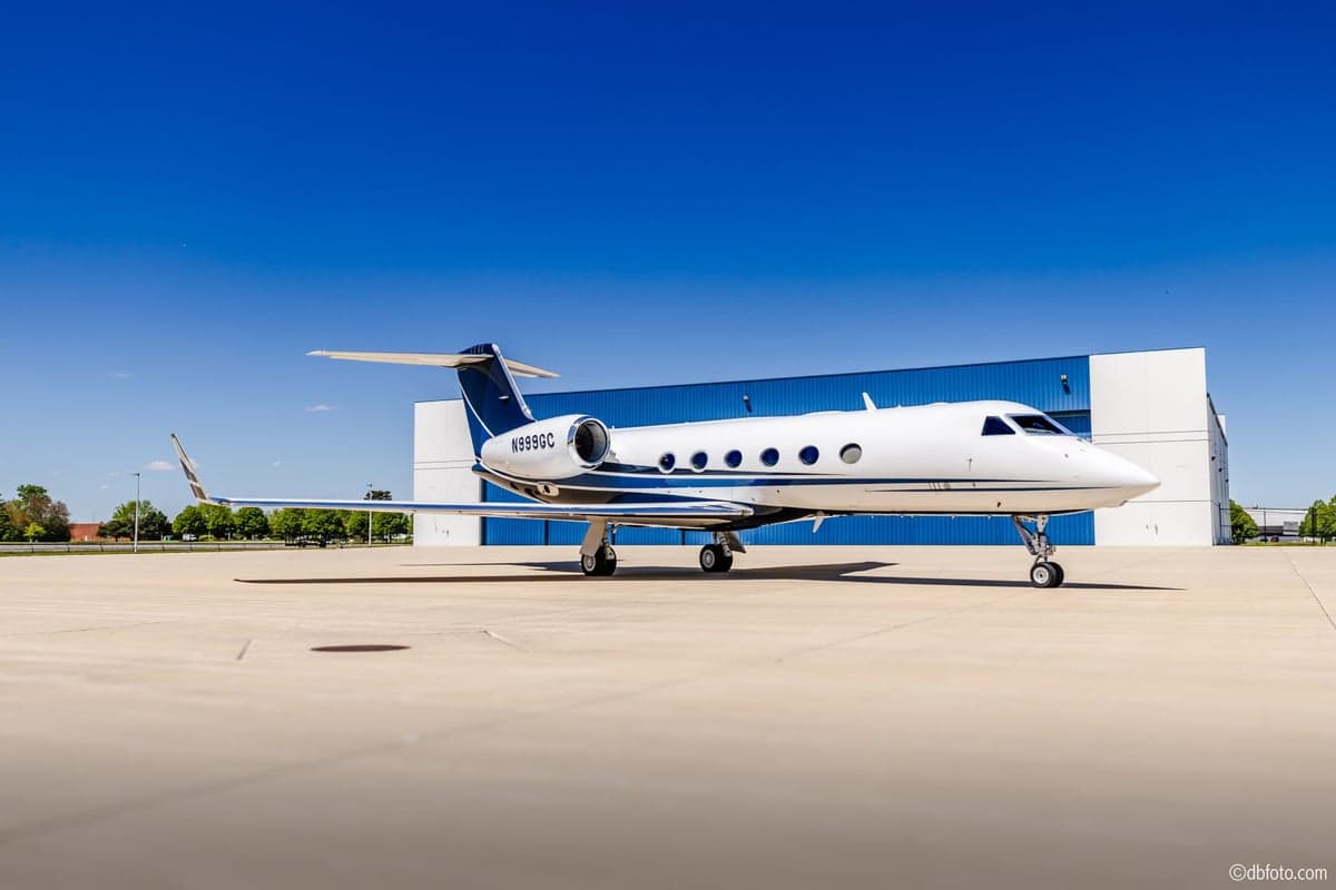 The N999GC Gulfstream G550 business jet, white with blue and black stripes, parked in front of a blue hangar.