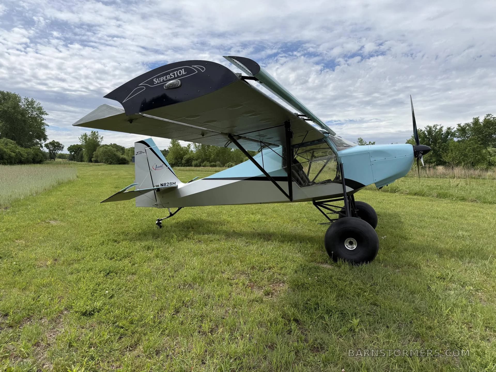 A rear-right view of a light blue and grey Just Aircraft SuperSTOL with 'SUPERSTOL' on the wing, parked on a grassy field.