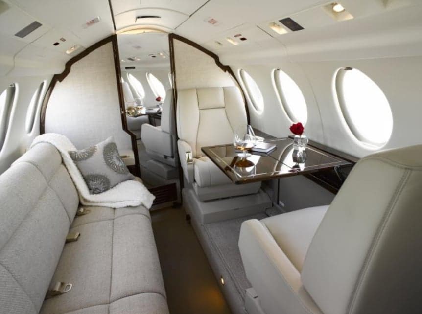 The interior of the aircraft features white leather seats and a couch with a decorative pillow.